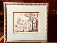 Framed etching showing the full artwork with wooden carved frame on a wood backdrop.