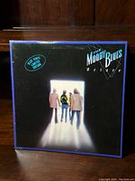 Front cover of the album showing four band members walking into a bright light with blue border and band and album title text