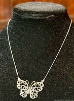 Necklace displayed on a black felt stand showing full chain and butterfly pendant in natural light, highlighting the delicate filigree and craftsmanship of the silver pendant.