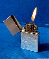 Front angle of Zippo 1933 style replica lighter with lid open and flame lit on a blue velvet background.