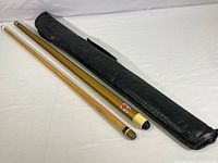 Full view of two-piece disassembled pool cue alongside black zippered leather carrying case laid out on white surface.