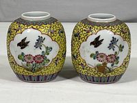 Photo showing front side of two small matching yellow vases decorated with pink flowers and a bird on each, intricate yellow swirling patterns in the background.