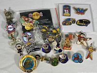 Top-down photo showing an assortment of about 20 collectible enamel pins, including Hard Rock Cafe, Planet Hollywood, Alaska, Disney, and racing themed designs.