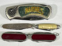 Photo of five collectible pocket tools laid out on a white surface, showing closed condition and details of Marines knife and smaller tools.