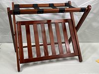 Front side view of wood folding luggage rack showing slatted lower shelf and black straps on top surface.