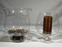 Both glass candle chimneys shown with decorative stones in larger chimney and brown candle in smaller chimney on pedestal base.