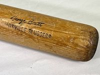 Close-up of the barrel end of the bat showing the "George Brett" and "Louisville Slugger" branding on the wood surface with wear marks and scratches.