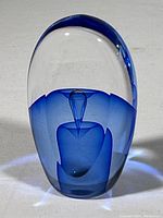 Full view of oblong glass paperweight showing the smooth transition from clear to blue glass and the central air bubble detail inside.