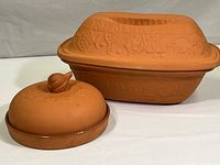 Photo showing both terra cotta cookware pieces: the garlic baker (front) and the rectangular Romertopf roasting dish (back)