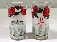 Two souvenir glasses with textured red rose designs and printed winners from past Kentucky Derby races, one with clear glass, the other frosted glass, both marked 1986 event.