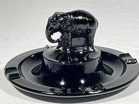 Close-up front view of black glass elephant ashtray showing detailed elephant figure and 3 cigarette rests on rim.