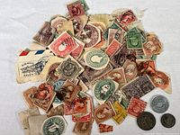 Photo showing a pile of assorted vintage postmarked U.S. stamps removed from envelopes, along with three coins: French 1 franc, another French coin, and a State of Washington tax token.
