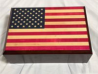 Closed wooden music jewelry box with an American flag design on the lid laid flat on a white cloth.