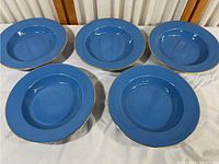 Set of five blue bowls with gold rims displayed on a white surface, showing general appearance and condition.