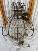 Full view of the hanging chandelier showing metal frame, multiple rows of large faceted crystal beads inside, and curved metal arms at the top with hanging crystal drops.