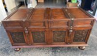 Photo of the dark brown wooden cocktail table with closed top showing carved decorative panels on front and bun feet.