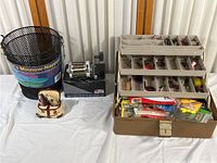 Photo showing the full collection including the Abu Garcia Ambassadeur reel on its box, the minnow trap, fish salt and pepper shakers, and the open tackle box full of fishing accessories.