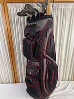 Full view of black and red Tourtrex golf bag holding several golf clubs of various brands including Titleist, Orlimas, and K & J.