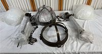Photo showing multiple metal hanging light parts including circular frames, chains, and bubble-wrapped glass covers spread on a white surface.