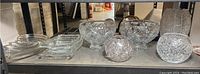 Photo showing a variety of cut glass bowls, plates, and candy dishes on a shelf including a large crystal bowl, smaller bowls, and square plates.