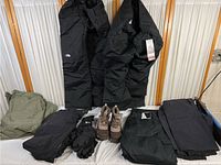 Overview of the lot showing multiple black insulated winter pants and jackets from The North Face, Helly Hansen, plus brown women's size 7 winter boots and black gloves.