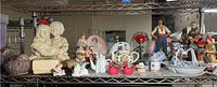 Wide shot of assorted porcelain and glass figurines, salt and pepper shakers, teapots, and decorative pieces on metal shelves, showcasing variety of sizes and styles.