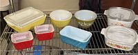 Full view of collection showing various sized Pyrex and CorningWare glass and ceramic bakeware, some with lids, in yellow, white, blue, and red including clear glass lids and floral pattern dishes.