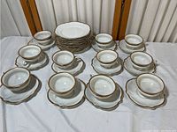 Full view of 11 cups, 11 saucers (coasters), and 11 plates arranged on a white cloth showing the set size and condition.