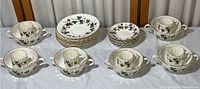 Full set view showing stacks of large and small saucers, alongside cups arranged on a table with grapevine pattern and gold edging.