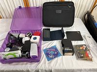Full collection of electronics on table including Samsung Galaxy S7 box, purple storage box with cables and accessories, black laptop sleeve, CDs and small electronics.