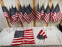 Wide shot showing 10 US stick flags arranged vertically on sticks and 2 flags lying flat on table.