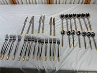 Full set of flatware arranged including knives, forks, and spoons with gold-dipped ends on handles.