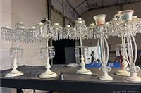 Set of five vintage white metal and composite candlestick holders with clear hanging crystal prisms, shown together on a table.