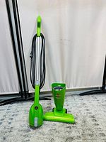 Front view of BISSELL Easy Vac stick vacuum with detachable hand vacuum and power cord coiled on side, on carpet floor with curtain backdrop.