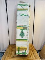 Box of the artificial Christmas tree, showing exterior with some damage and tape, green tree image on box