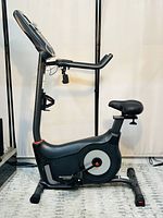 Full side profile of the upright bike showing seat, pedals, and digital console.