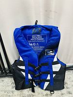 Front view of blue and black adult small life jacket showing three buckle straps and brand label.