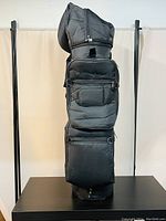 Front view of a black golf bag showing zippered storage compartments and protective cover at the top.