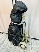 Golf bag with multiple compartments mounted on used two-wheeled metal golf cart with white wheels, standing upright on patterned floor