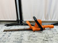 Side view of orange electric hedge trimmer showing rusted dual-blade cutting head, black handle, and orange rear grip.