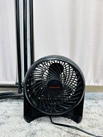Front view of black circular compact Honeywell desk fan showing grille and brand name.