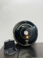 iRobot Roomba robot vacuum cleaner next to black charging dock/base on black surface against white background.