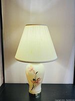 Front view of the working ceramic table lamp with floral design under white fabric shade.