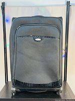 Front view of the large black luggage bag featuring a large zippered front pocket with textured black faux leather accent and fabric body.