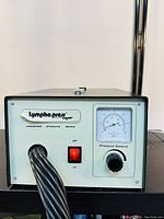 Front panel view of Lympha Press device showing brand label, cable coil, red on/off switch, and analog pressure gauge.