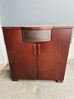 Front view of the wooden dresser cabinet with closed doors and drawer, showing the dark wood finish and metal handles.