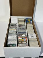 White 3-row storage box filled with assorted sports cards packed and sorted in rows with some cards sleeved and some loose.