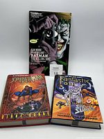 Photo of the 3 hard cover comic books standing and stacked on a white surface.