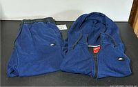 Full view of the folded blue Nike tracksuit jacket and pants laid flat, showing color and texture.