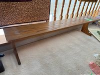 Full side view of the long oak bench on carpet showing the natural wood grain and flat seating surface.